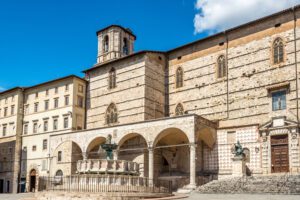 Vista scorciata dell'esterno della cattedrale di San Lorenzo. La facciata su Pizza IV Novembre si mostra nella sua imponenza, e allo stesso tempo nella sua incompiutezza. Ai piedi delle scalette che portano all’ingresso si trova la Fontana Maggiore.