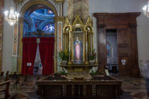 Vista frontale della Madonna delle Grazie all'interno della Cattedrale di San Lorenzo. Questa si trova all’interno di una cornice lignea dorata addossata a una colonna e che la abbraccia interamente. Ai suoi piedi, degli spazi per inginocchiarsi per la venerazione.