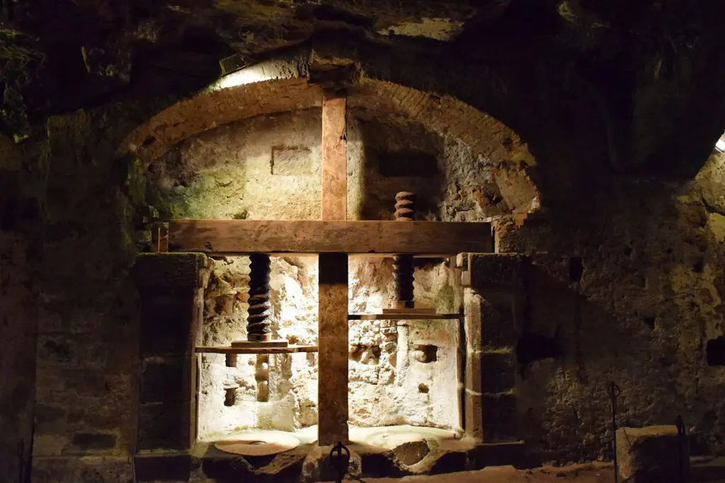 Vista frontale di un’antica pressa da vino, illuminata dall’alto, situata nell’Orvieto Sotterranea.