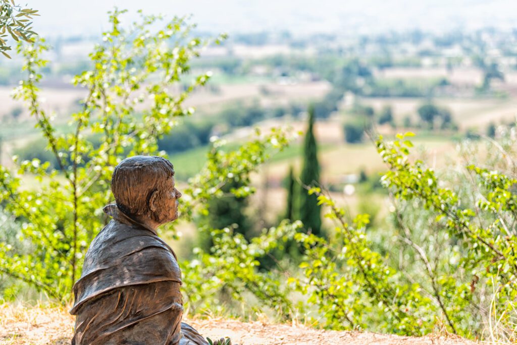 Vista del profilo della statua di San Francesco seduto a pregare. Questa statua, situata vicino alla chiesa di San Damiano, guarda alle campagne umbre.