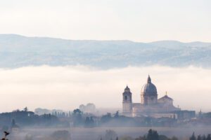 Vista panoramica di Santa Maria degli Angeli. La struttura della chiesa, con il suo cupolone, si erge dalle campagne umbre e spicca dalla nebbia della piana in cui si trova.