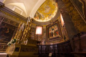 Vista scorciata dell'abside della Cattedrale di Città della Pieve. Sulla sinistra l'altare con i candelabri, sulla destra l'abside affrescato e al cui centro campeggia il quadro con la Madonna in trono con Bambino.