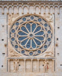 Dettaglio del rosone principale sulla facciata della Cattedrale di Santa Maria Assunta. Il rosone circolare è inscritto in un quadrato, sorretto dal due statue, mentre negli 4 spazi tra gli angoli del quadrato e il cerchio sono contenuti i simboli degli evangelisti.