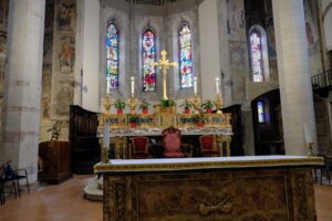 Altare della chiesa di San Francesco a Gubbio. Sull’altare decorato con oro, si erge un crocifisso in oro. Sullo sfondo le vetrate dell’abside.