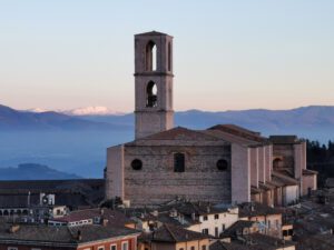 Vista in lontananza dell'imponente Basilica di San Domenico. La struttura svetta enormemente sull'abitato, con il suo campanile che si protende verso il cielo. Sullo sfondo il paesaggio montano visibile da Perugia.