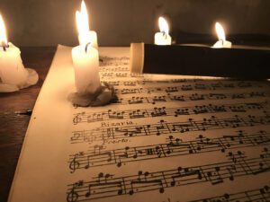 Su uno spartito musicale appoggiato su di un tavolo sono poste delle candele accese che ne illuminano le note con una calda luce.