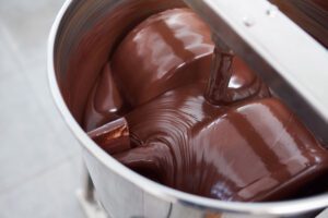 Vista ravvicinata di un contenitore in acciaio all'interno del quale del cioccolato fuso viene mescolato automaticamente.