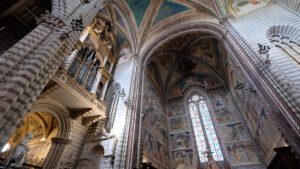 Vista dal basso dell’abside del duomo di Orvieto. Le pareti sono interamente affrescate con le storie della vita di Maria. Sulla sinistra è visibile l’organo della chiesa.