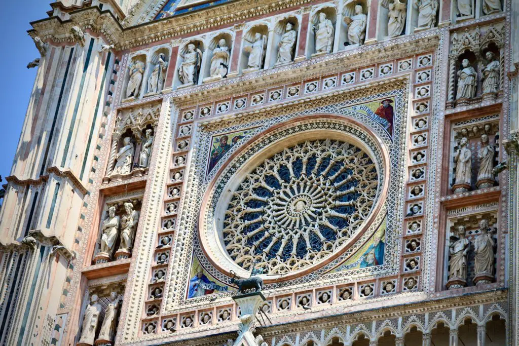 Dettaglio del rosone della facciata del Duomo. Il rosone è inscritto in una cornice quadrata e circondato da sculture di marmo con apostoli e profeti. Al centro del rosone è scolpito il volto di Cristo.