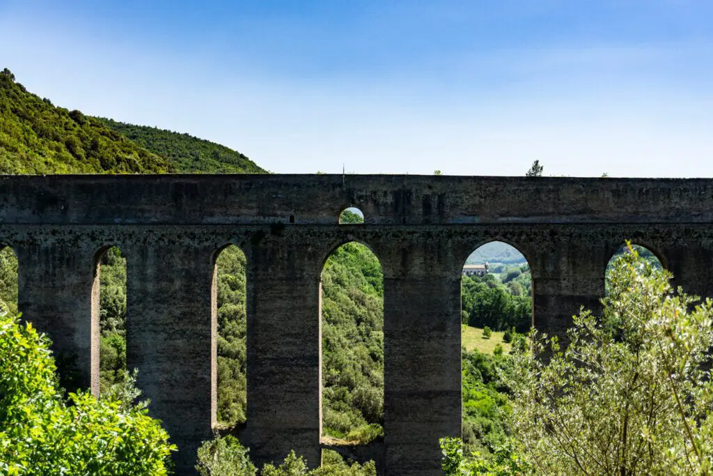 Vista frontale delle grandi arcate del Ponte delle Torri di Spoleto. I quattro archi visibili si aptrono come grandi finestre sul verde circostante mentre il ponte è sormontato dal cielo azzurro.