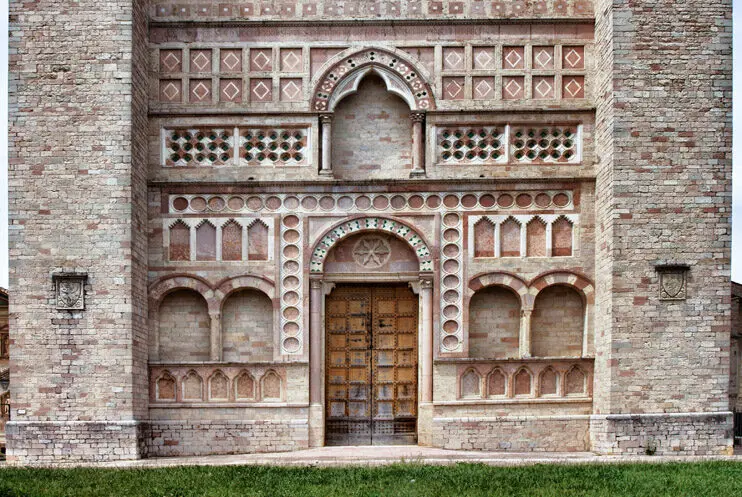 Vista frontale della parte bassa della facciata di San Francesco al prato. Al cento il portale di ingresso, incorniciato da decorazioni scultoree geometriche e archi. La facciata, in pietra rossa, ha inserti di colore turchese.