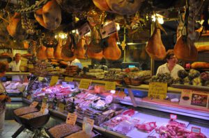 Vista dell'interno di una norcineria di Norcia. Salumi e prosciutti pendono dal soffitto come decorazioni, mentre il bancone è ricolmo salsicce, salami e affettati tipici umbri.