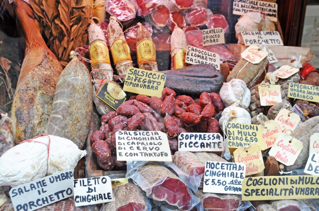 Selezione di salumi tipici umbri esposti nella vetrina di una norcineria. Salami, salsicce secche,coglioni di mulo e vari insaccati abbondano.