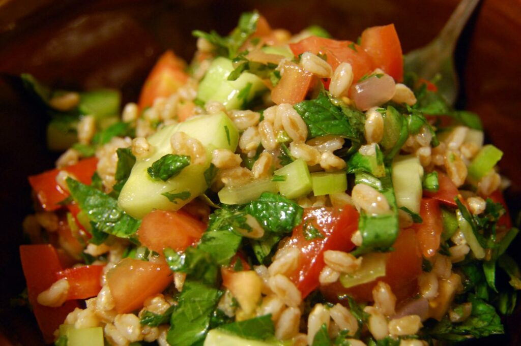 inquadratura ravvicinata su in piatto con un’insalata fredda di farro. Il farro è condito con cetrioli, pomodori e basilico.