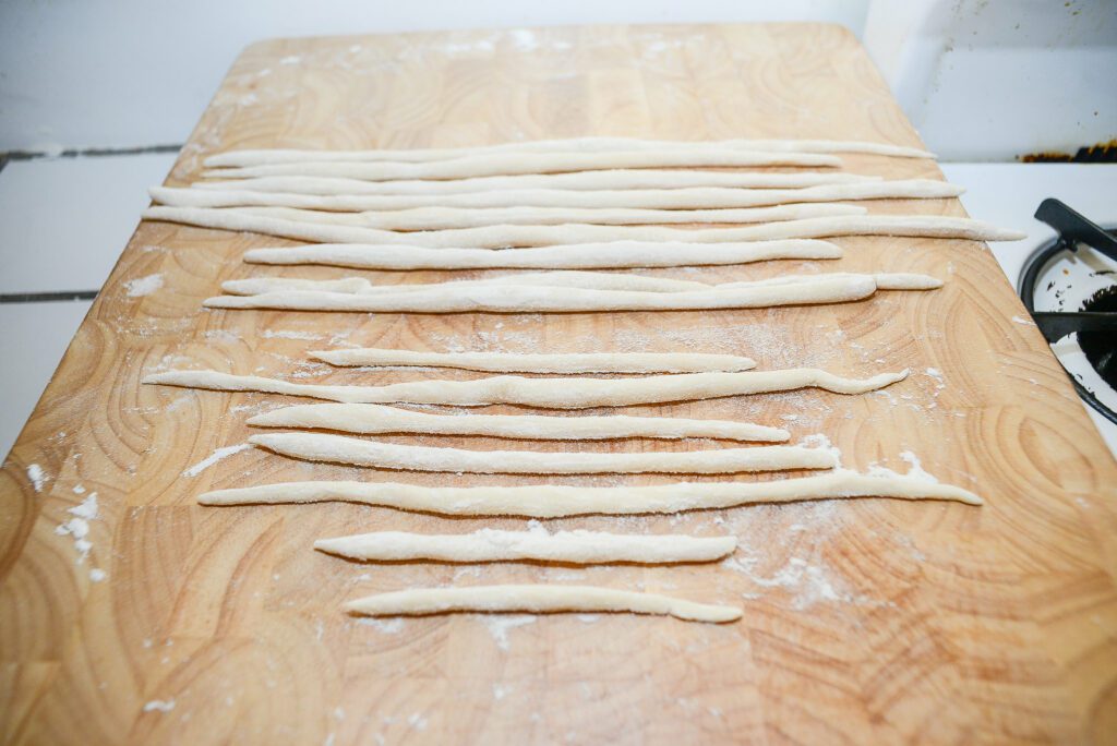 Ampia inquadratura di un tagliere di legno con sopra degli umbricelli fatti a mano. La pasta ha la sua forma tipica: lunga, arrotolata e spessa.