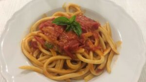 A shot from above of a plate of umbricelli seasoned with tomato sauce and a basil leaf as a decoration on the top.