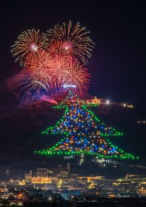 vista frontale dell’albero di Natale di Gubbio si trova sulle pendici del Monte Ingino, sopra la città di Gubbio. L’albero di Natale è fatto di luci a led che vengono accese ogni anno il 7 dicembre; questa foto è stata scattata durante il momento dell’accensione, segnato dai fuochi d’artificio. Sopra la punta dell’Albero è ben illuminata la Stella Cometa; accanto alla punta, sulla destra, è illuminata la Basilica di Sant’Ubaldo (il Santo patrono della città). Alla base dell’albero, invece, si trova la città di Gubbio.