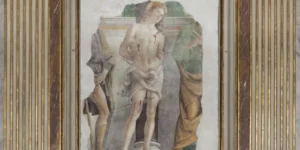 visione d’insieme dell’affresco. Al centro San Sebastiano legato a una colonna, con la testa e lo sguardo rivolti verso l’alto e il corpo trafitto da tre frecce, due sul petto e una sulla gamba destra. È completamente nudo, a parte un panno che gli copre i fianchi. Sulla sinistra parte di una figura umana che mostra una ferita sanguinante sull’interno coscia sinistro (presumibilmente San Rocco) con una tunica corta e un’altra sulla destra con una lunga tunica che tiene nella mano destra una chiave (probabilmente San Pietro).