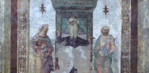 Detail of the fresco by Perugino entitled "Saint Anthony Abbot between Saints Paul the Hermit and Marcellus" and preserved inside the Church of Saints Peter and Paul in Città della Pieve. In the main scene, Saint Anthony Abbot is painted in the centre, seated on an elegant raised throne from which two lanterns hang. While looking intently at the observer, the Saint has his right hand raised and his left hand resting on his stick, an object with which he is usually depicted in sacred paintings. Saint Anthony Abbot is flanked by Saint Paul the Hermit and Saint Marcellus, as indicated by the inscription at the base of the throne. In 1861, an earthquake hit the church and damaged the fresco. The work was then transferred to a canvas and restored, but it was not possible to restore it to its original state due to colour fading in much of the artwork.