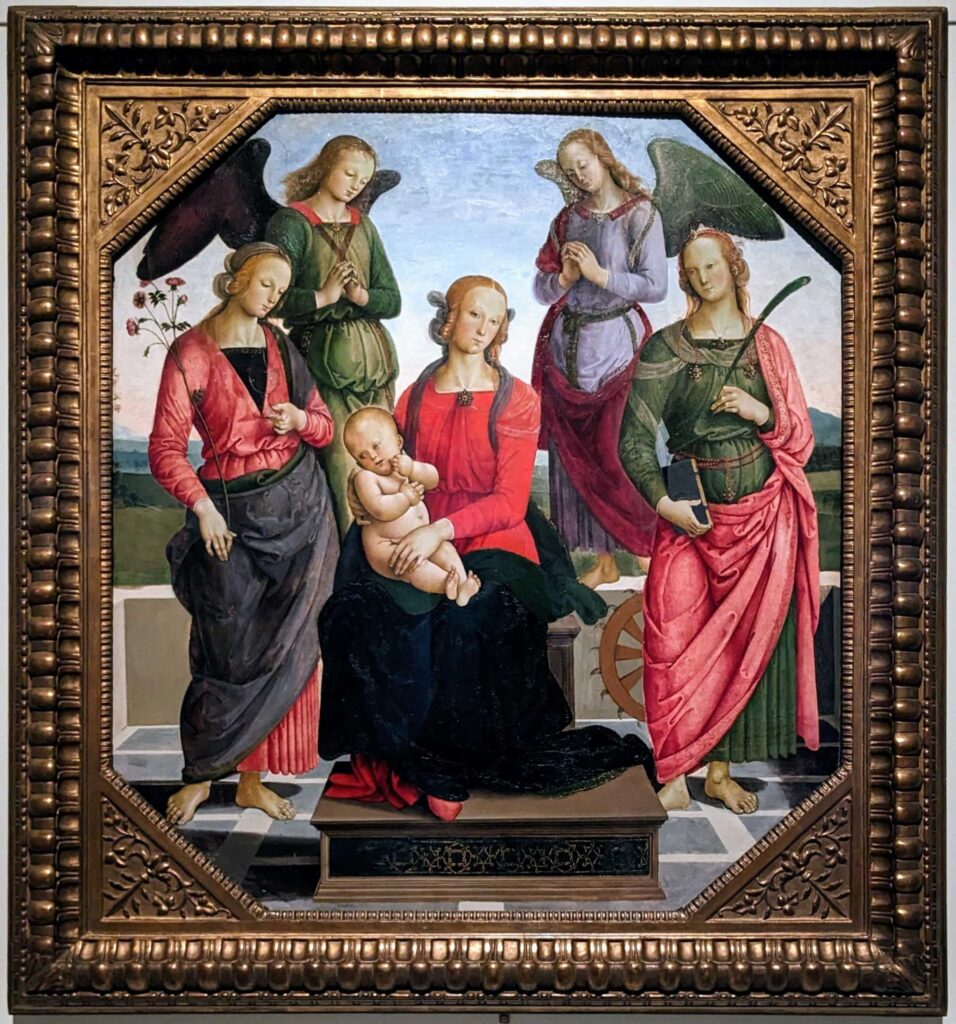 Opera del Perugino che raffigura al centro la Madonna col Bambino seduta su un trono, affiancata dalle Sante Rosa e Caterina d’Alessandria. Dietro di esse, due angeli oranti in posizione simmetrica poggiano sulla balaustra. Il paesaggio che fa da sfondo alla scena è formato da dolci colline e un cielo sereno.