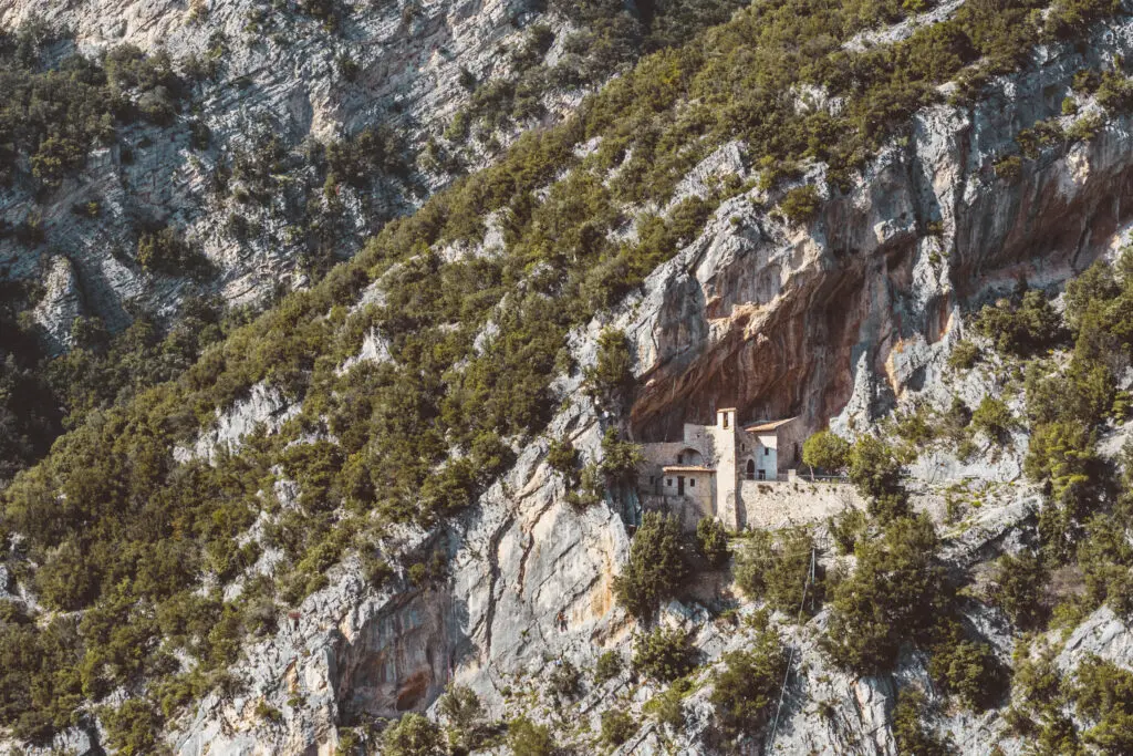 Vista frontale panoramica dell’Eremo di Santa Maria Giacobbe che si trova a Pale, vicino a Foligno, in Umbria. Il complesso religioso è stato costruito nella rientranza di una parete rocciosa del Monte Pale.